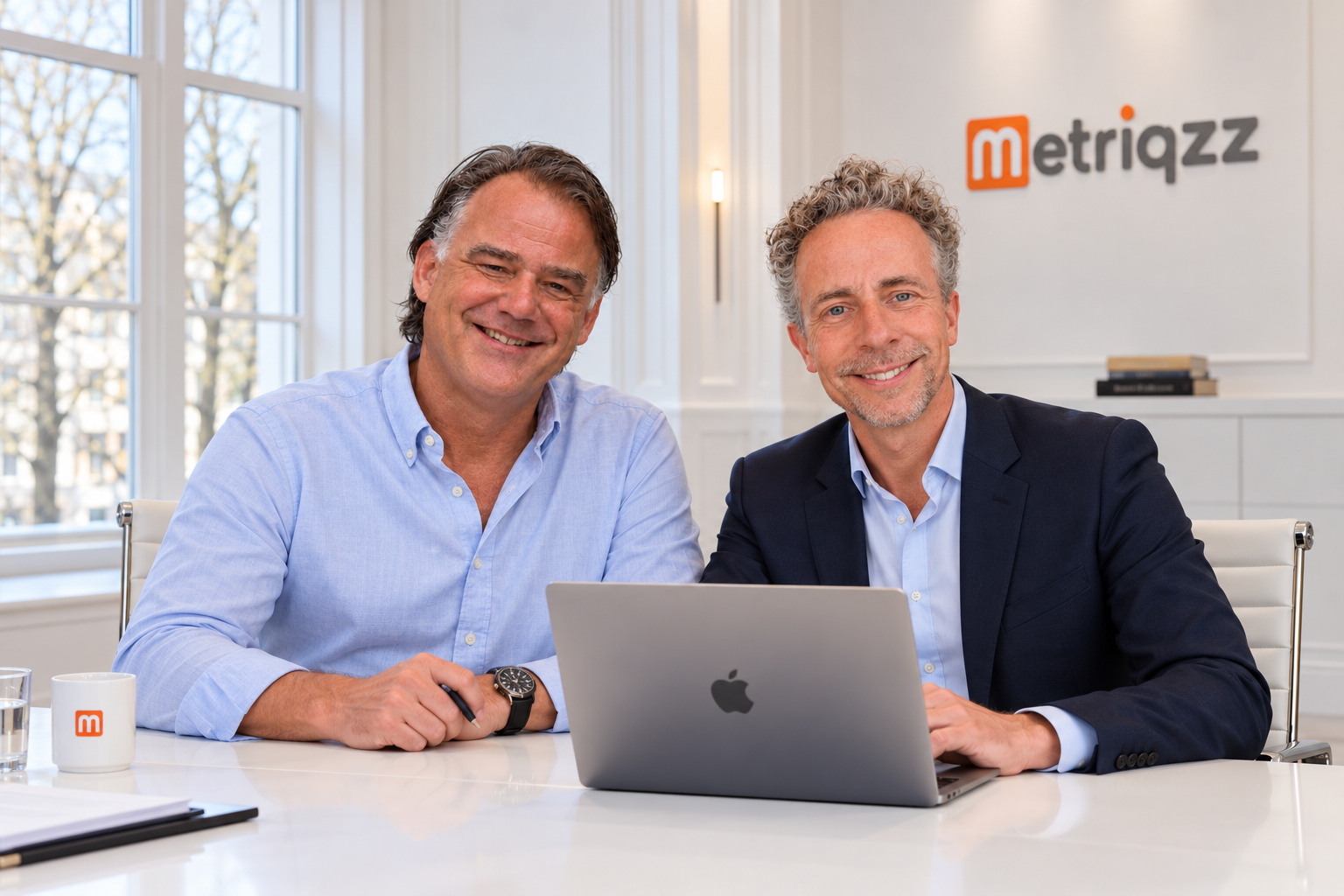 Twee oprichters van Metriqzz aan een vergadertafel met een laptop, voor het Metriqzz-logo